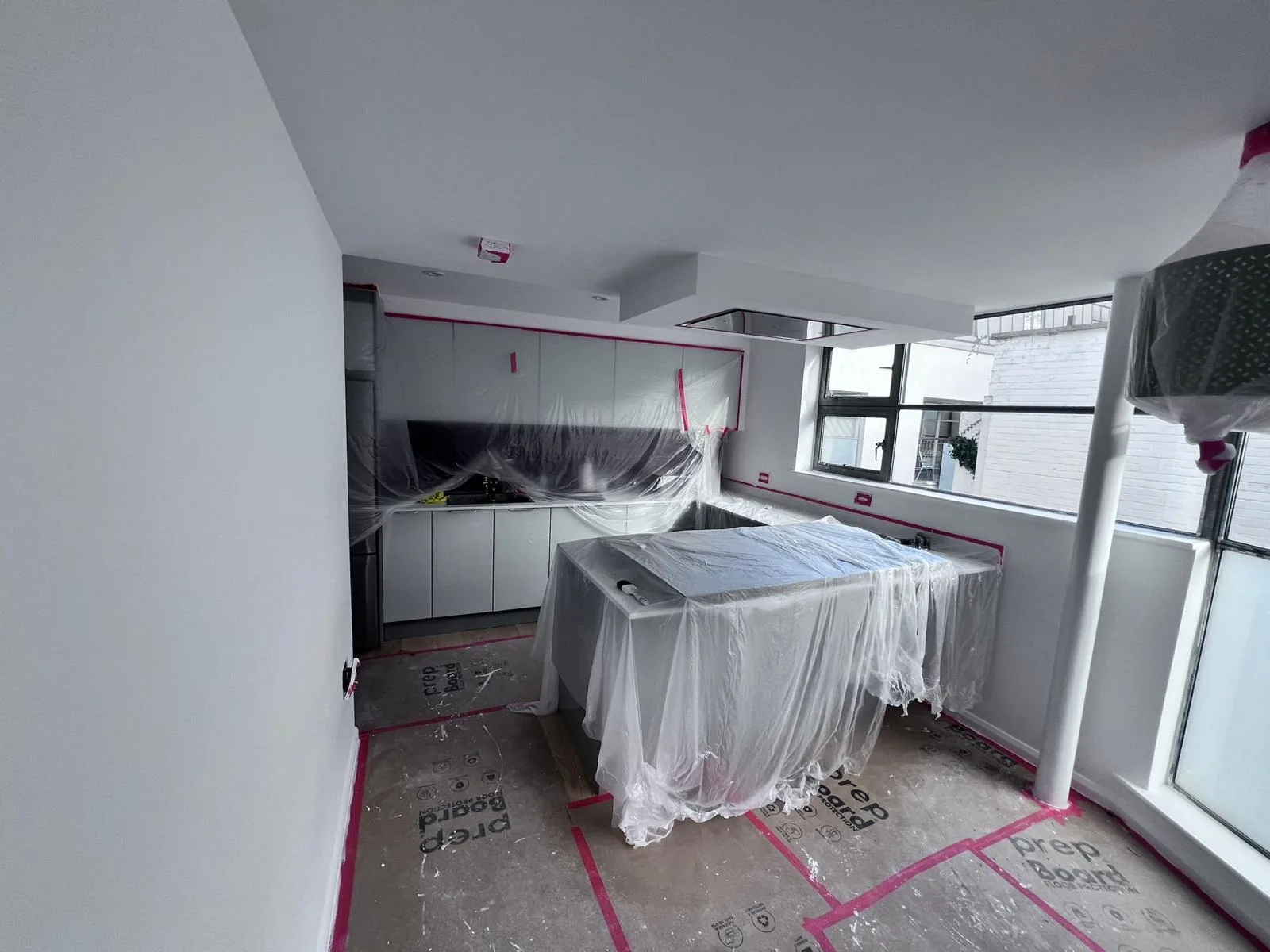 Kitchen masked and sheeted for spray painting with fresh white walls and ceiling