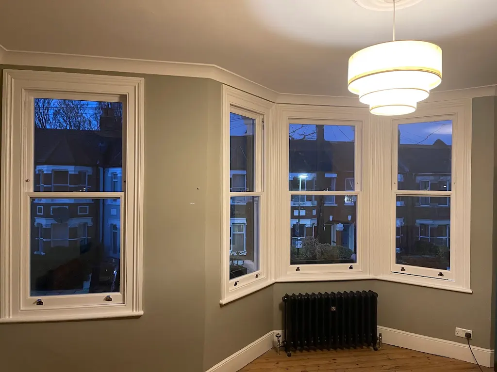Restored bay sash windows in a green period living room at dusk