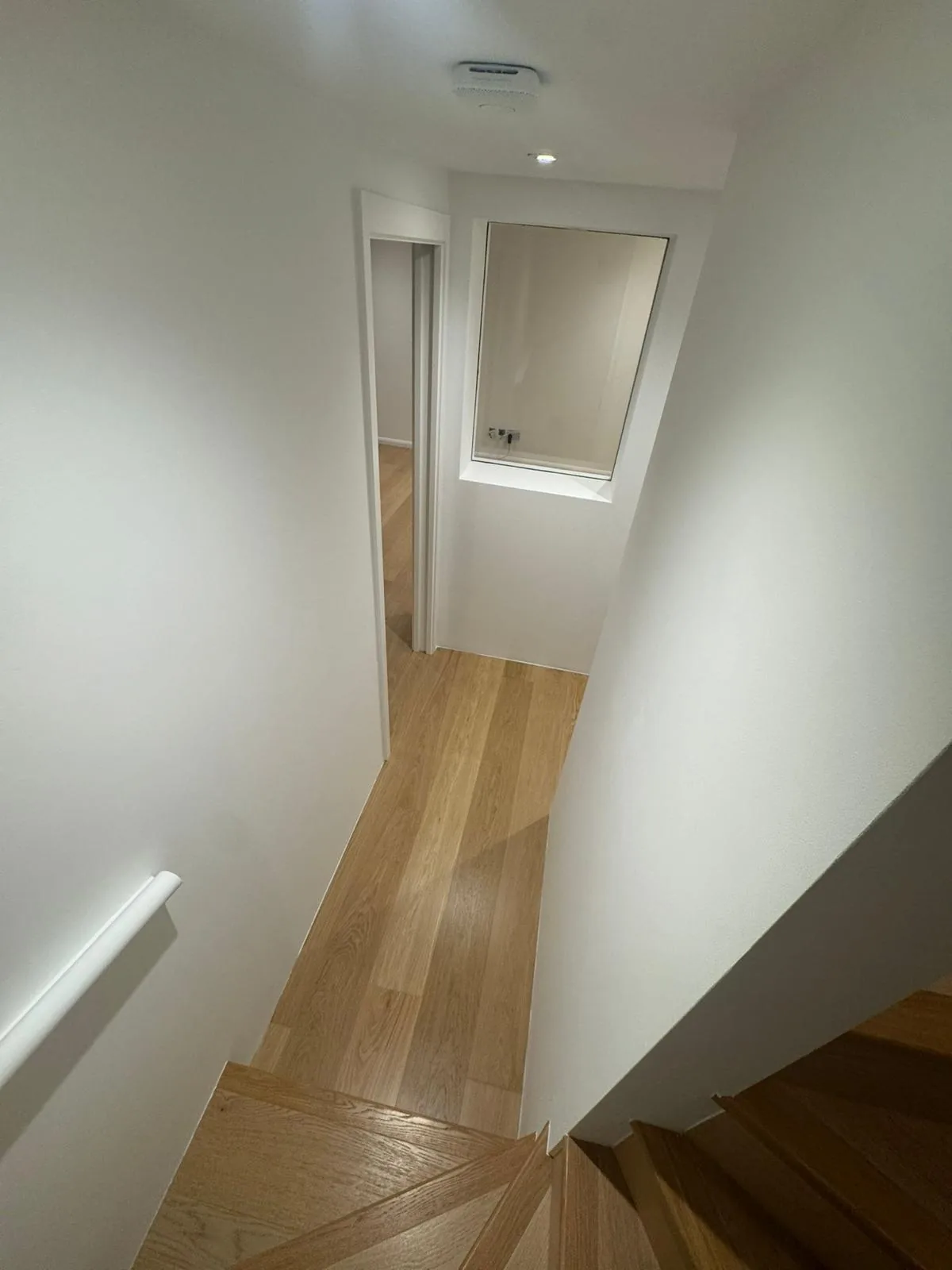 Freshly painted upper landing with internal glazed window over oak flooring
