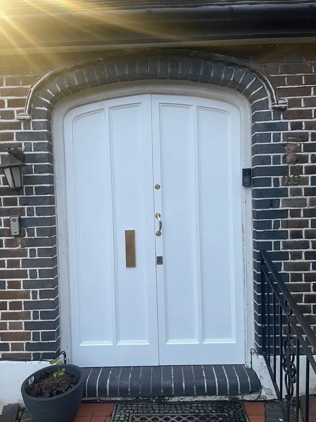 Repainted arched white double front doors on a red-brick Tudor-style home