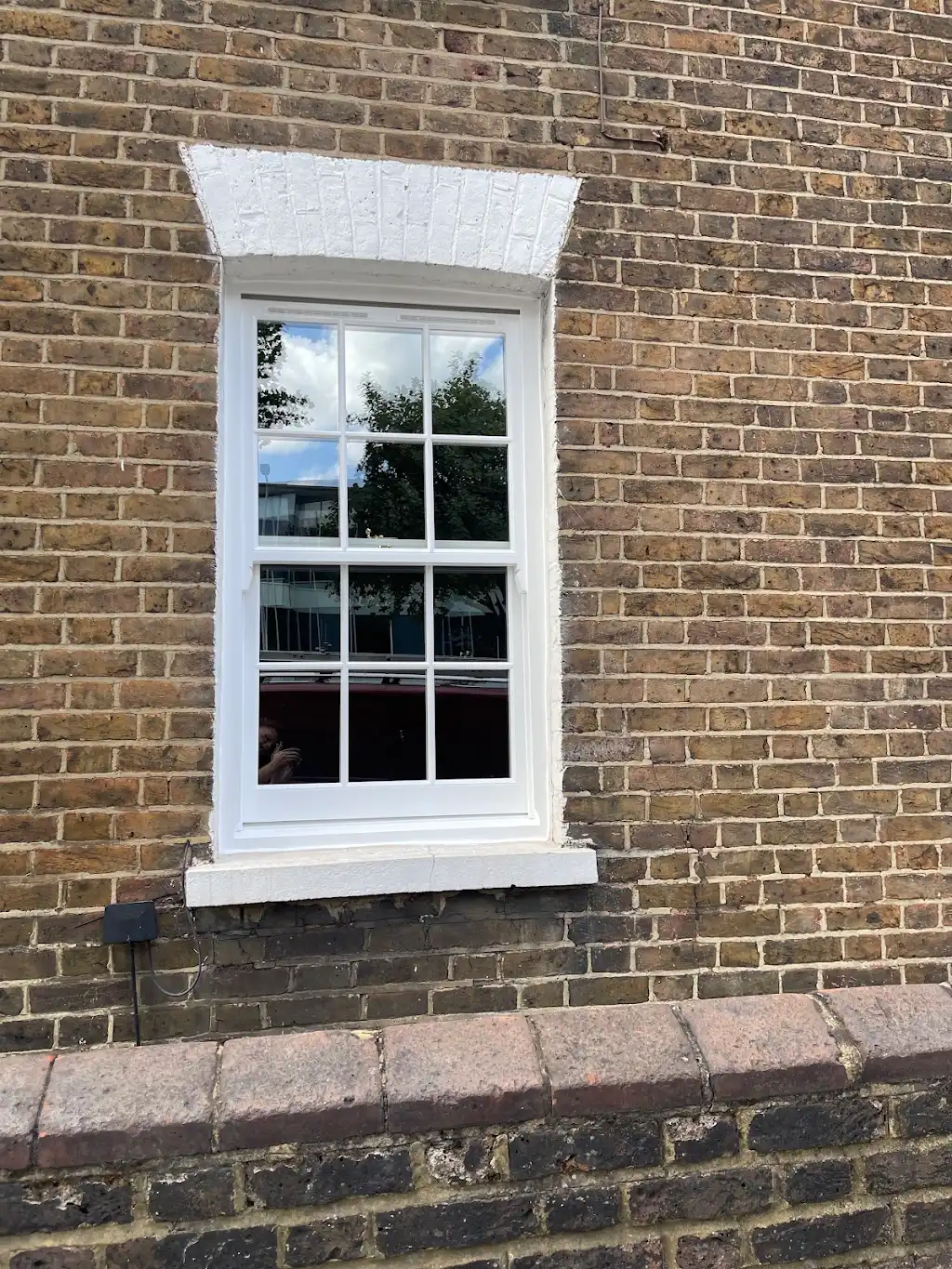 Restored white sash window with painted brick arch on a London townhouse