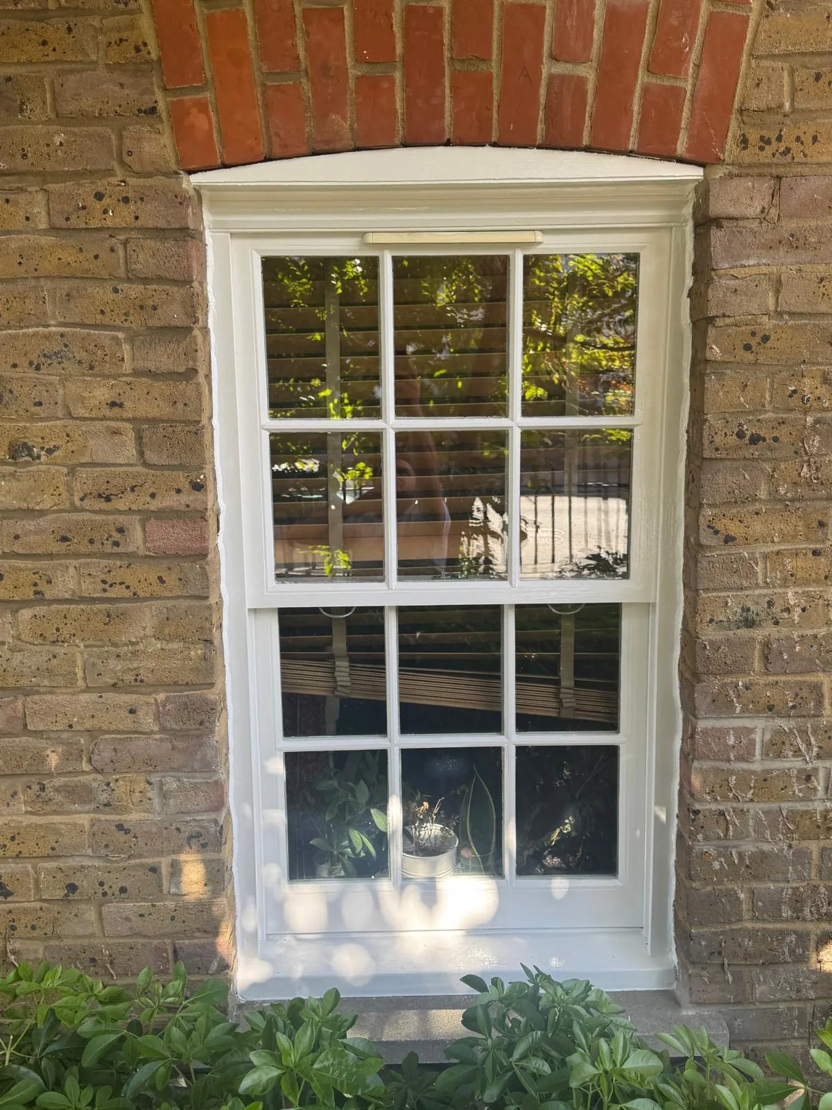 Restored sash window with brass sash lift above a garden bed on a London brick wall