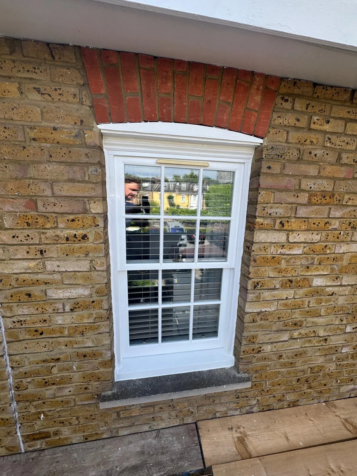 Repainted white sash window with red brick arch on a yellow London brick façade