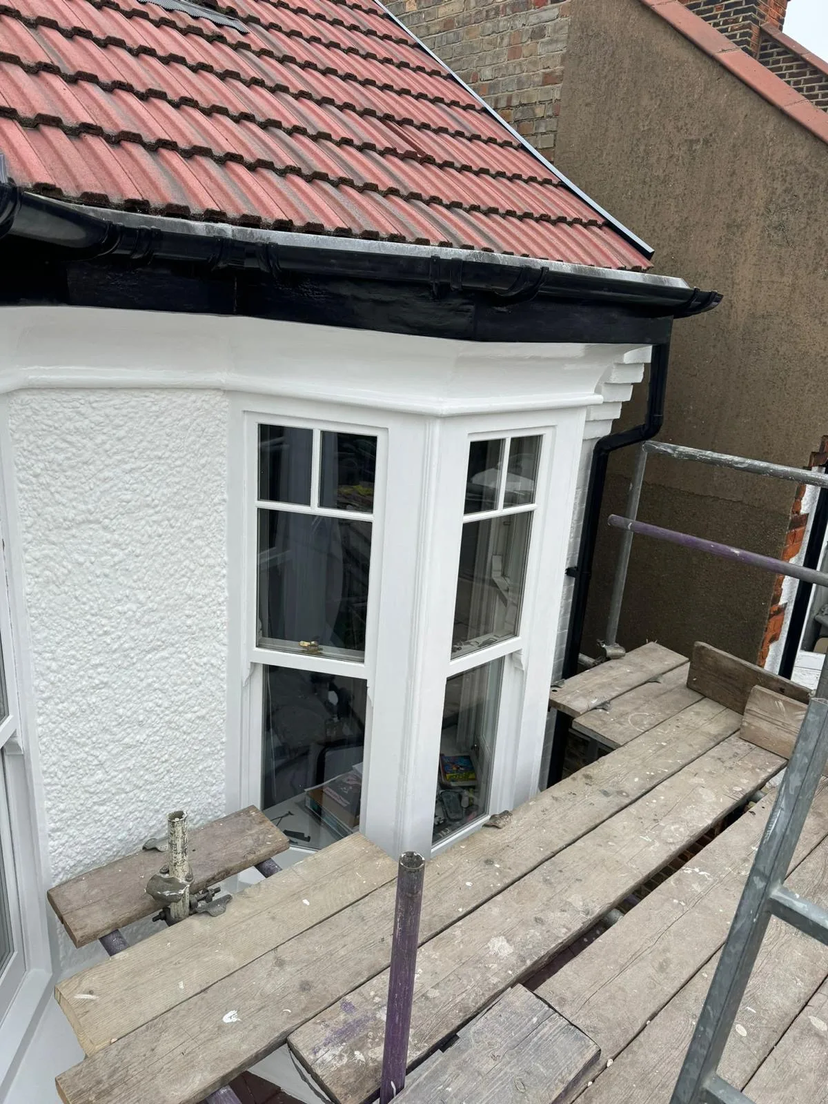 Restored white timber bay window with crisp gloss finish above a tiled roof