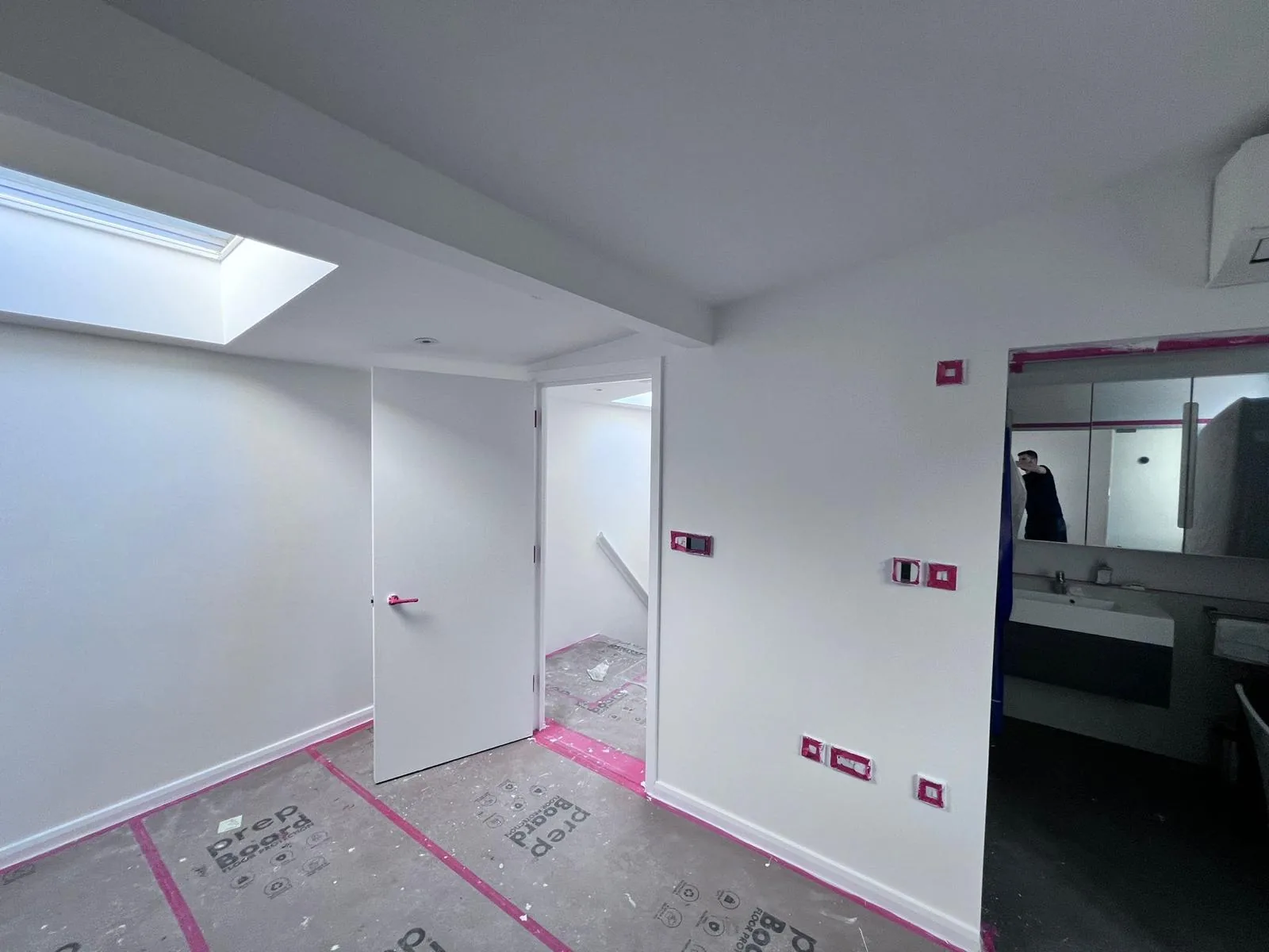 Loft room mid-decoration with fresh white walls, skylight and prep boards on the floor