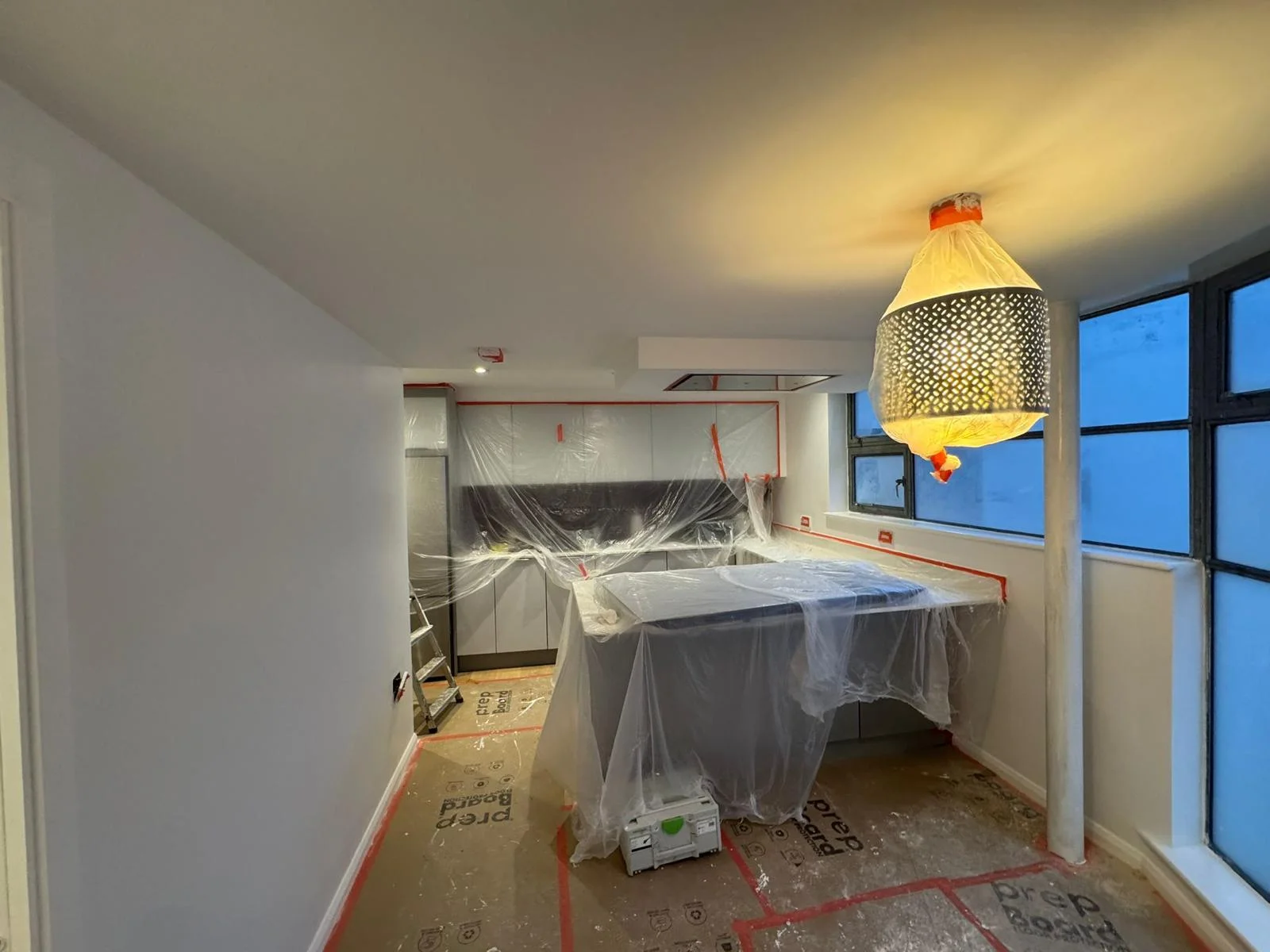 Kitchen masked and sheeted for spray painting with freshly painted white walls and ceiling