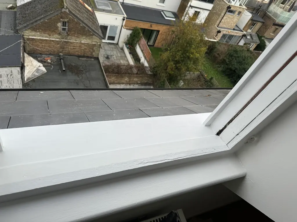 Freshly painted white loft sash window sill above slate roof
