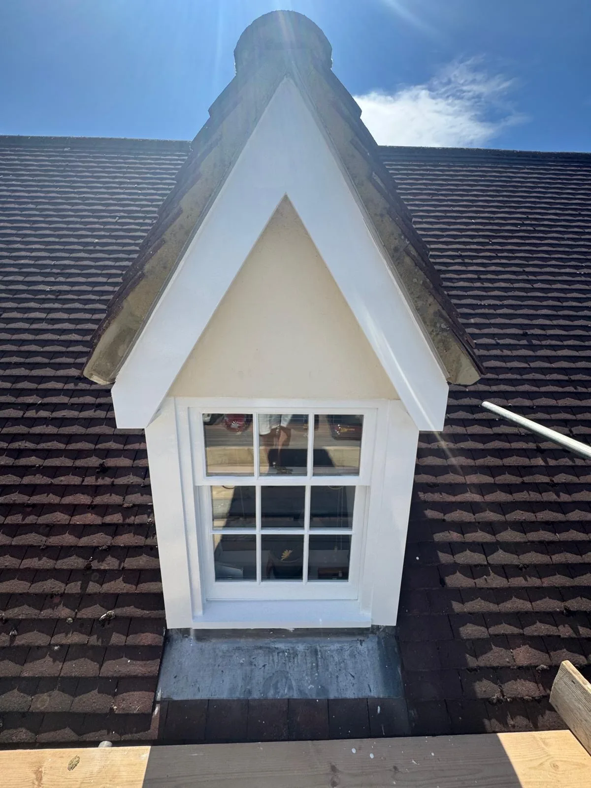 Repainted white gabled dormer sash window against a blue sky on a tiled roof