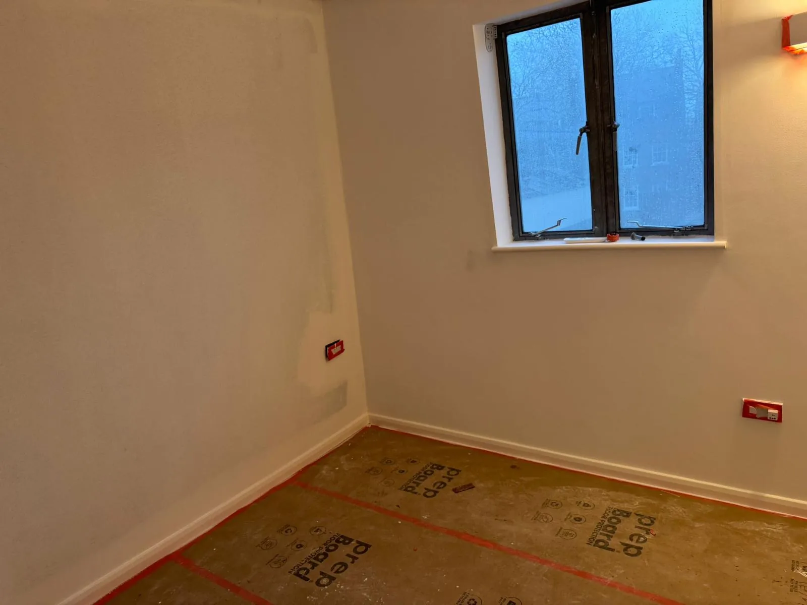 Compact bedroom freshly painted white with black casement window and floor protection