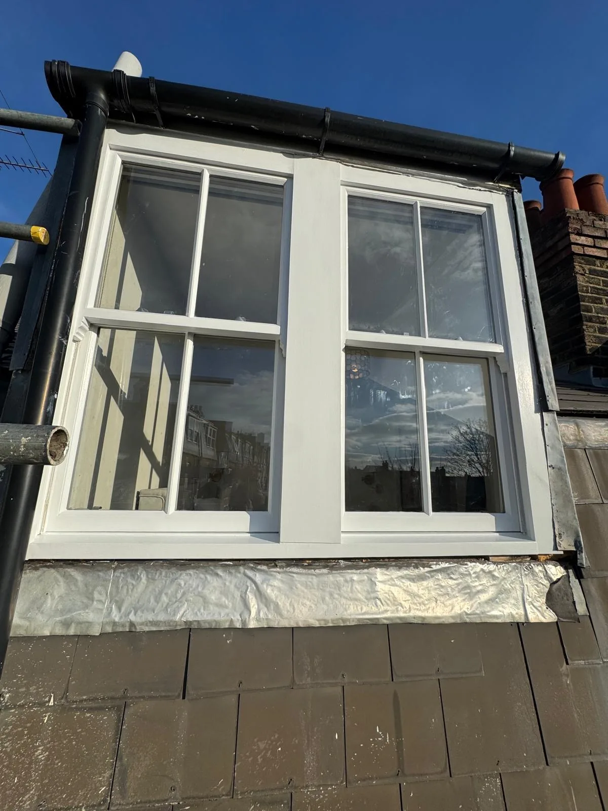 Twin sash dormer windows freshly repainted white against a blue sky