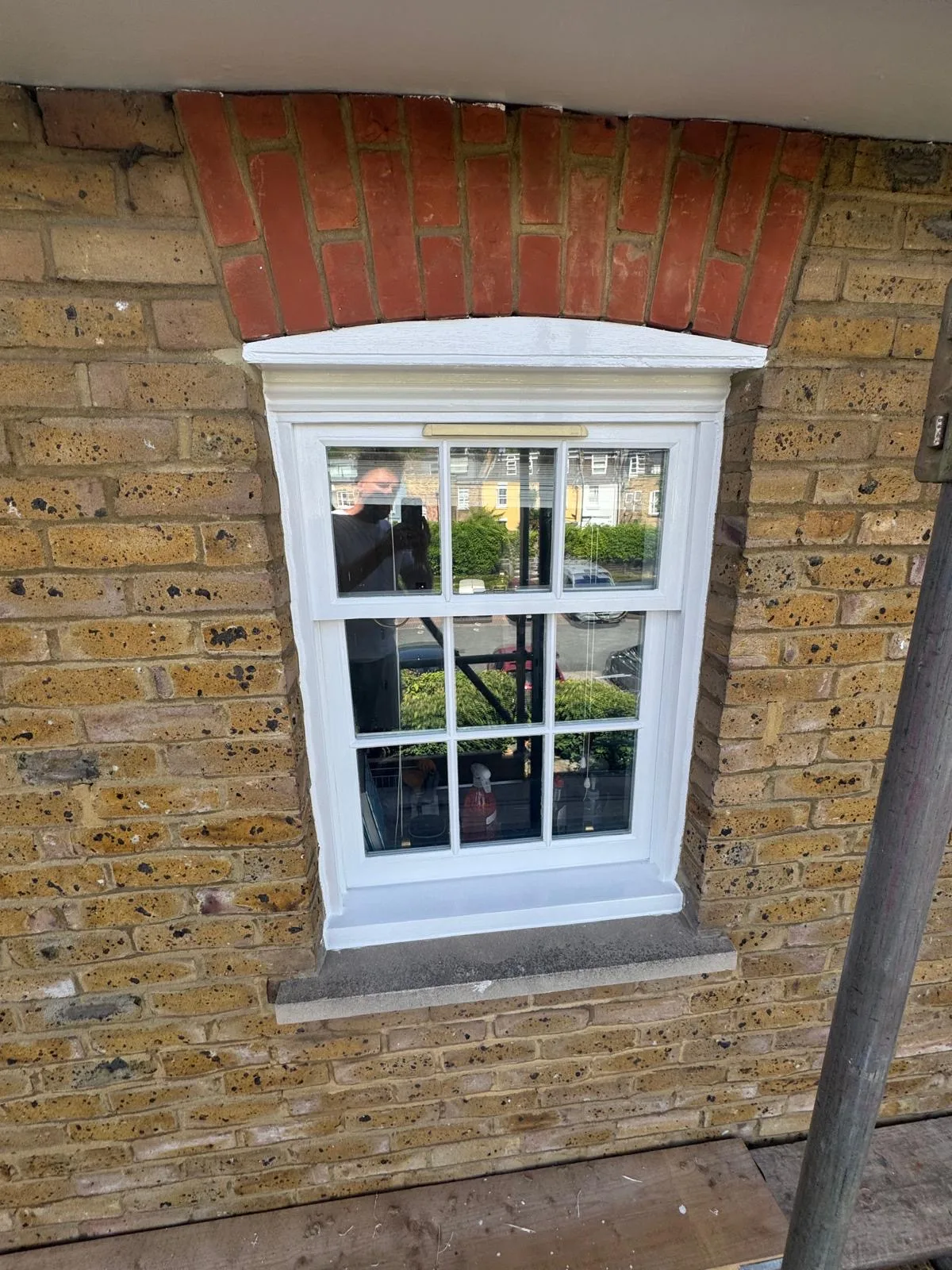 Repainted sash window with brass fittings and red brick arch on a stock brick wall