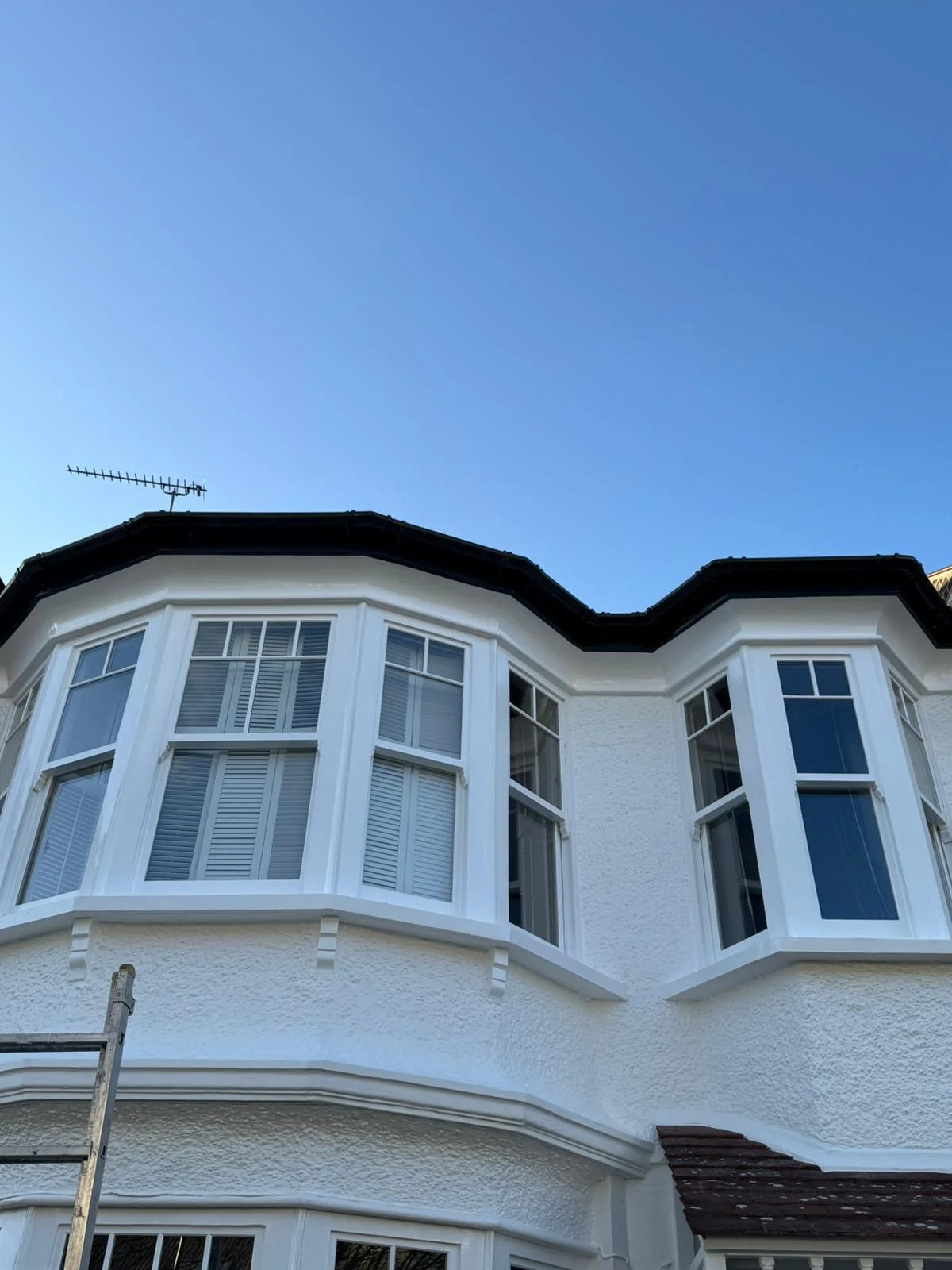 Finished exterior repaint of a Victorian bay window elevation in bright white against blue sky