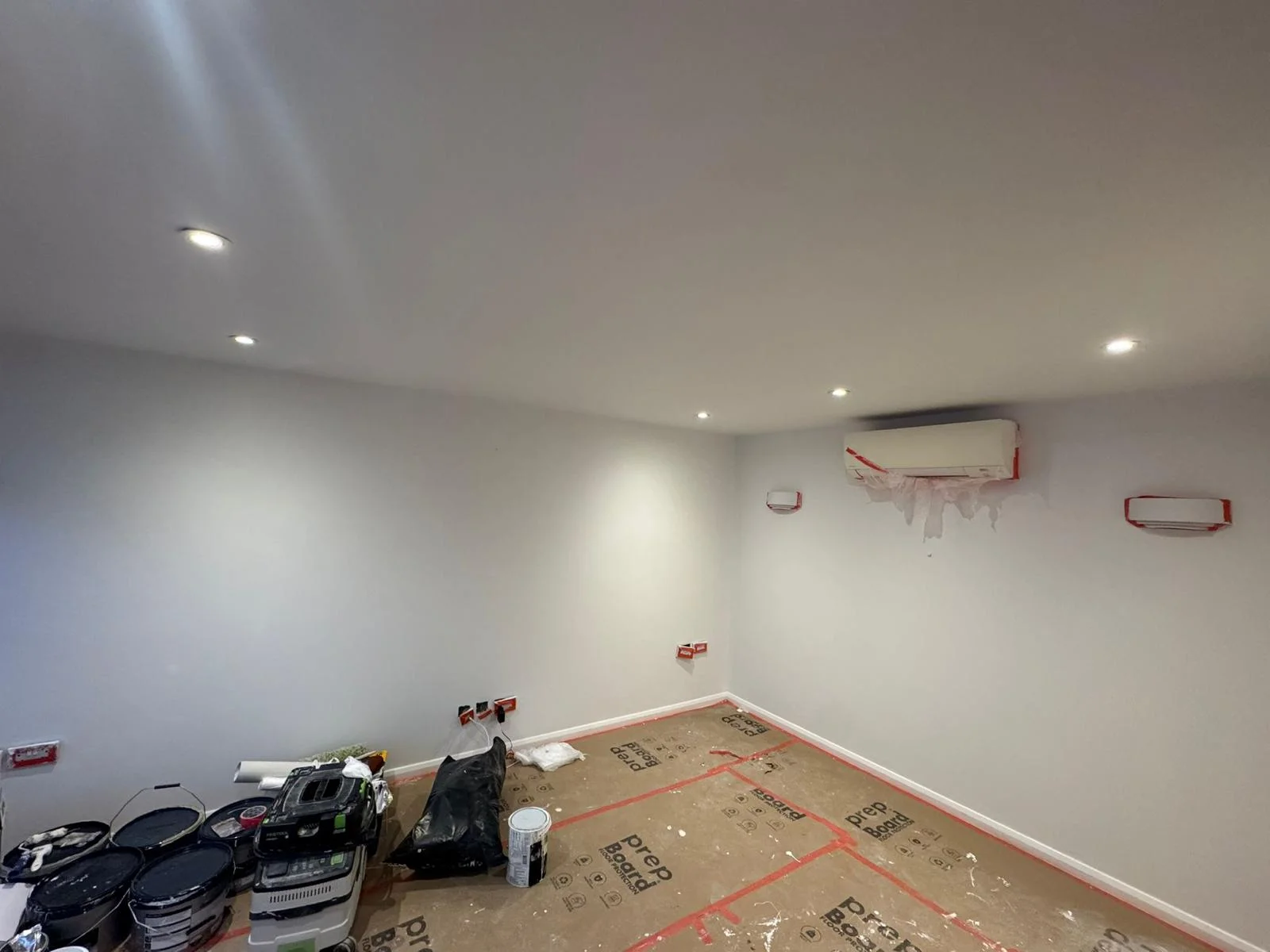Large room freshly painted white with recessed downlights and air-conditioning unit