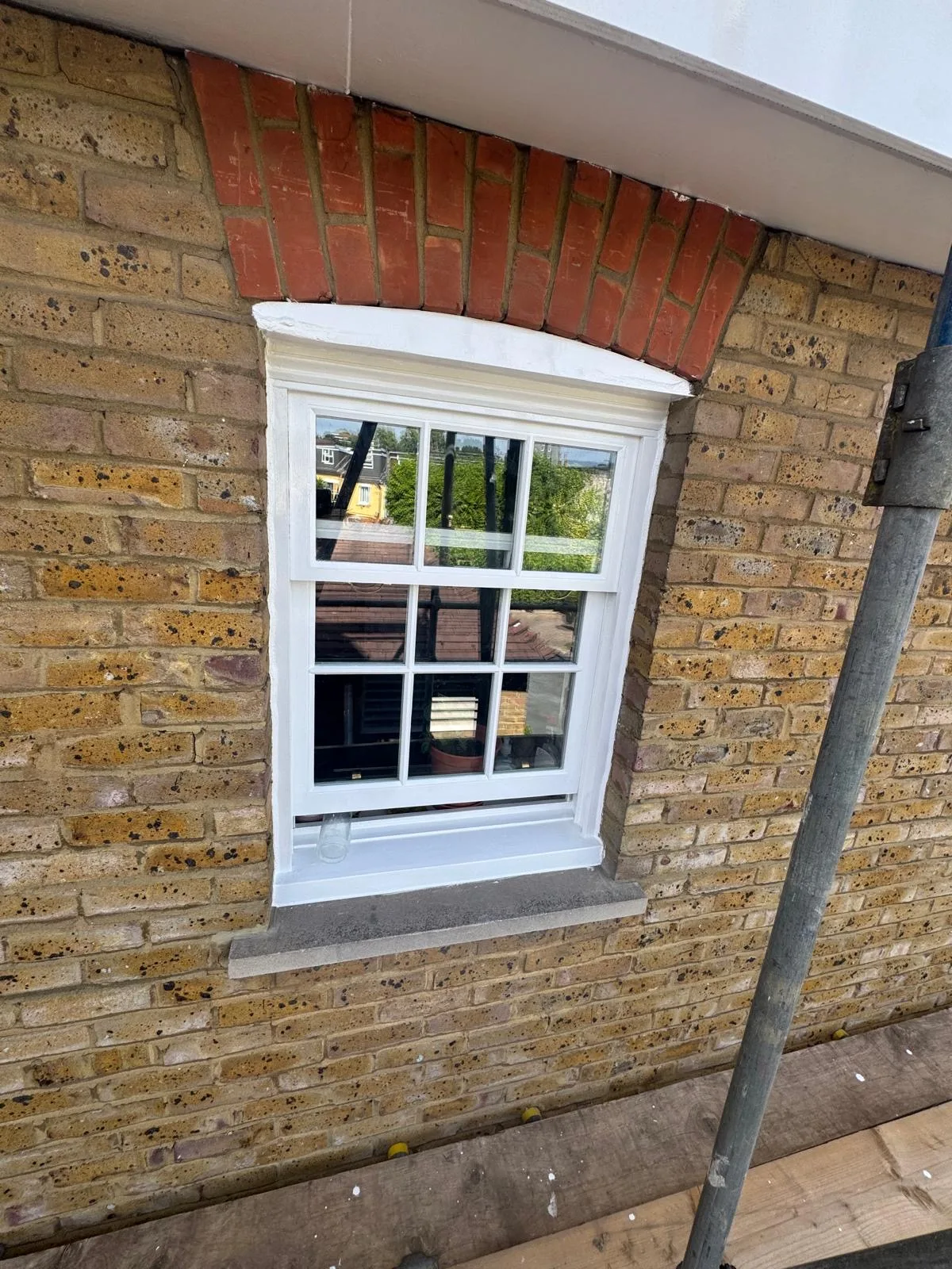 Freshly painted white sash window with red brick arch mid-scaffold restoration