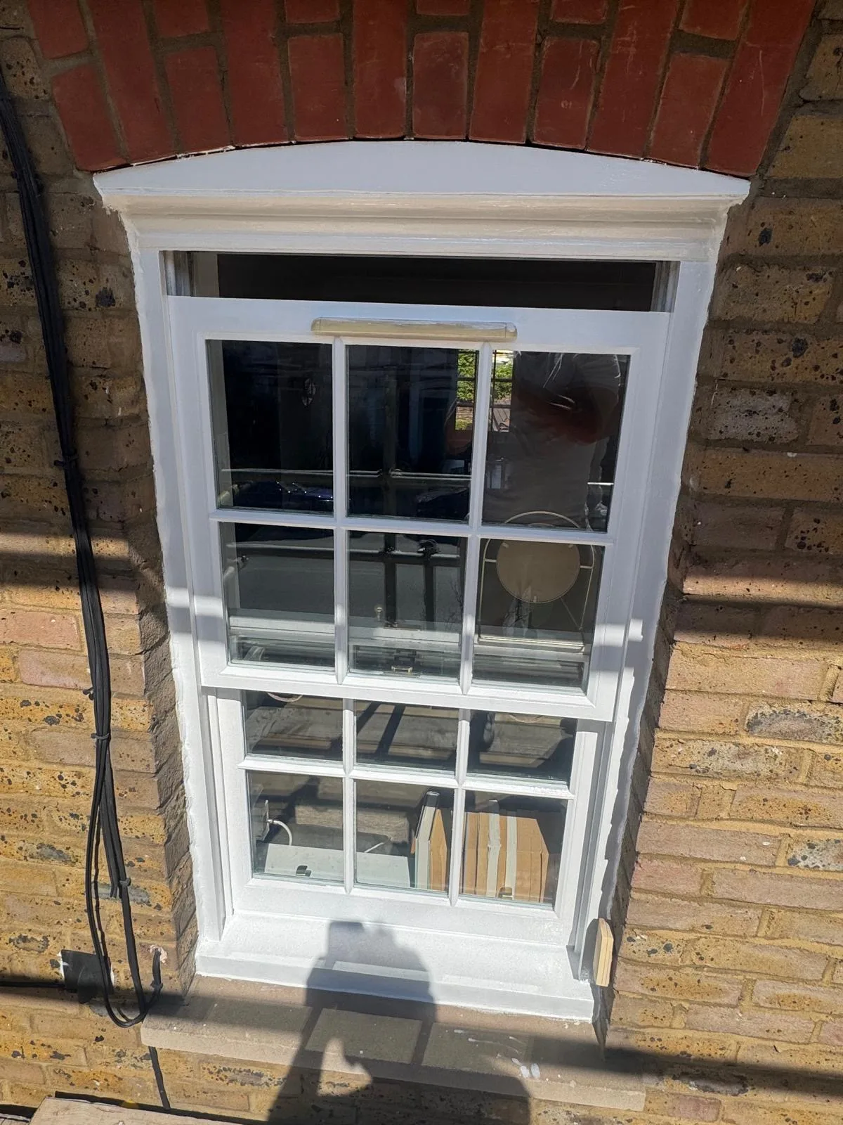 Restored white sash window with red brick arch on a London brick façade