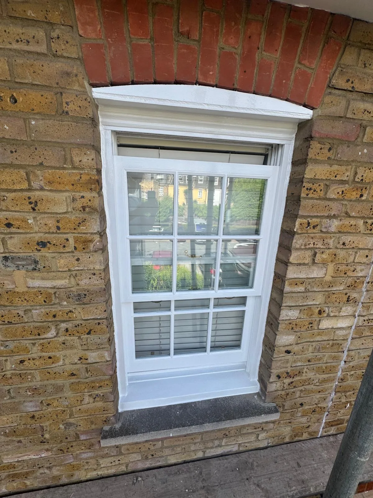 Freshly repainted white sash window with brass fittings on a stock brick façade