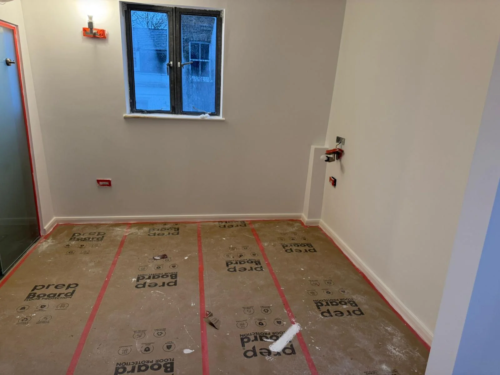 Compact room freshly painted white with black casement window and prep boards on the floor