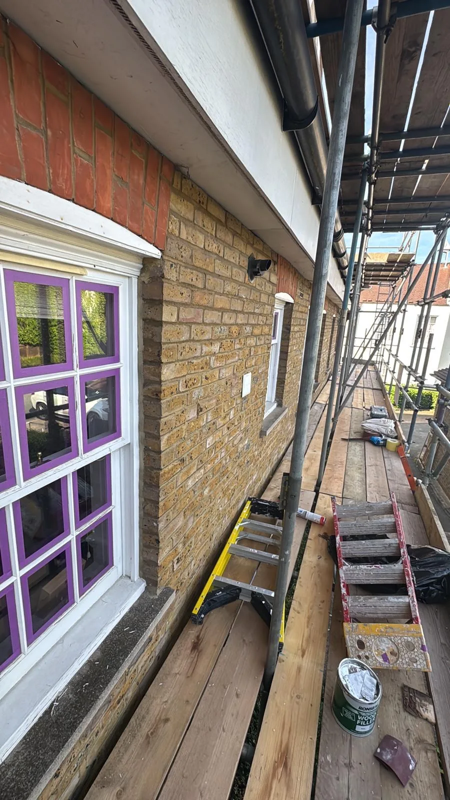 Sash window on London brick façade masked with purple tape mid-restoration