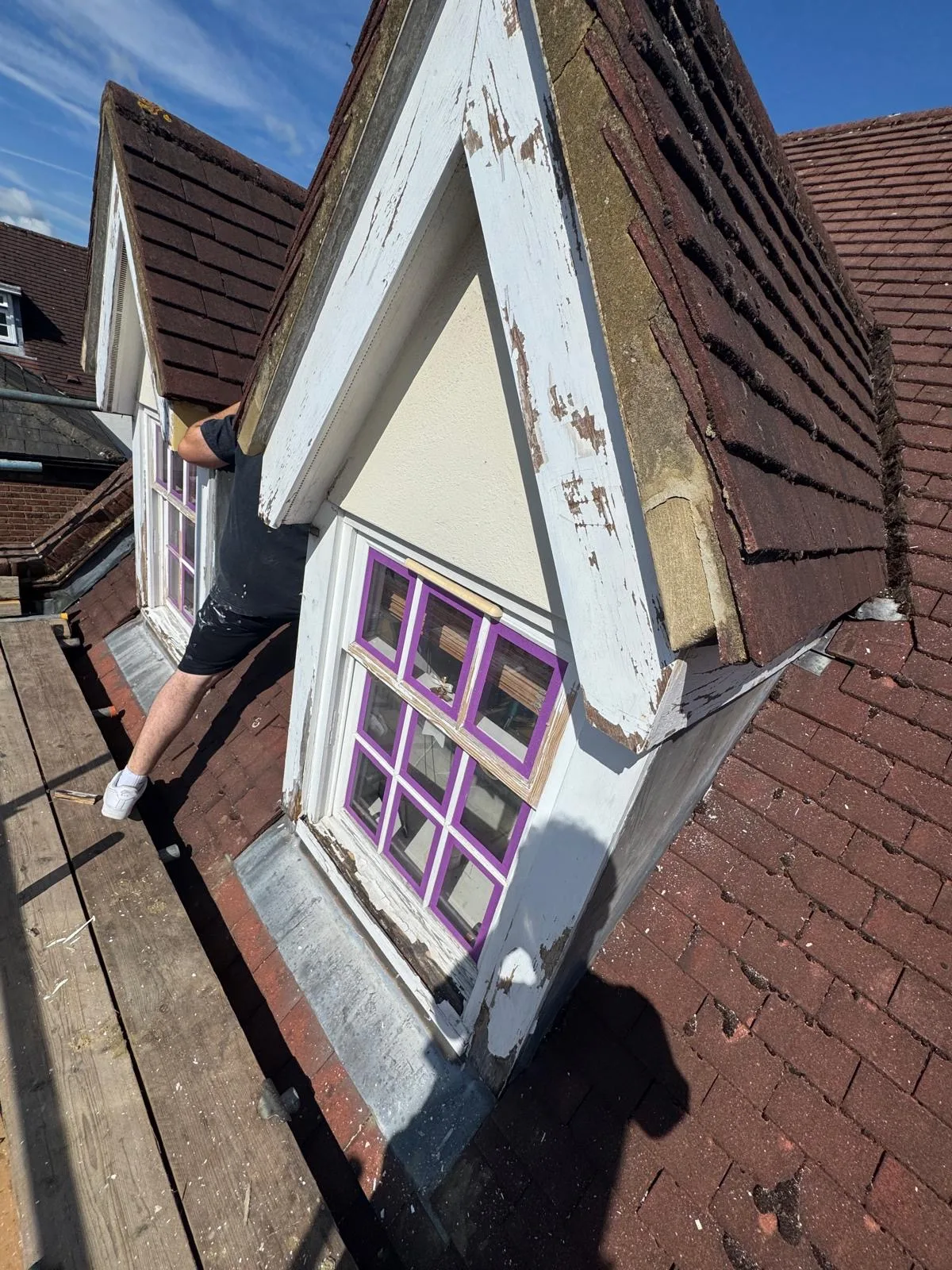 Twin gabled dormer windows on tiled roof mid-restoration