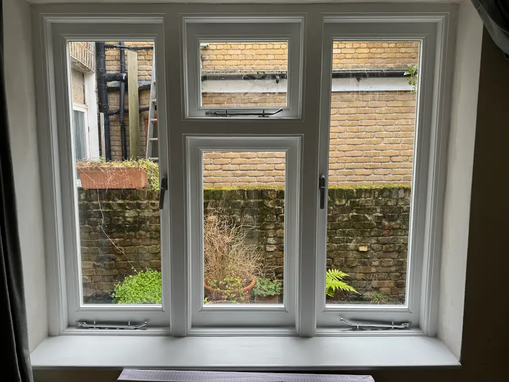 Restored interior casement window in soft grey overlooking a London garden
