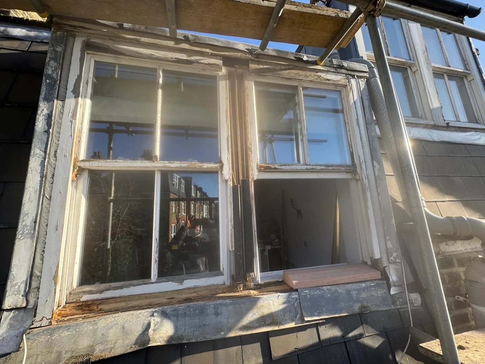 Twin sash window with peeling paint and rotted frames prepped for restoration from scaffold