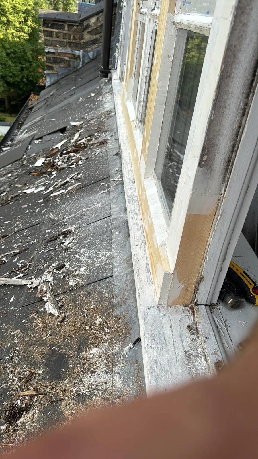 Sash window frame mid-repair with new timber inserts and stripped paint over slate roof