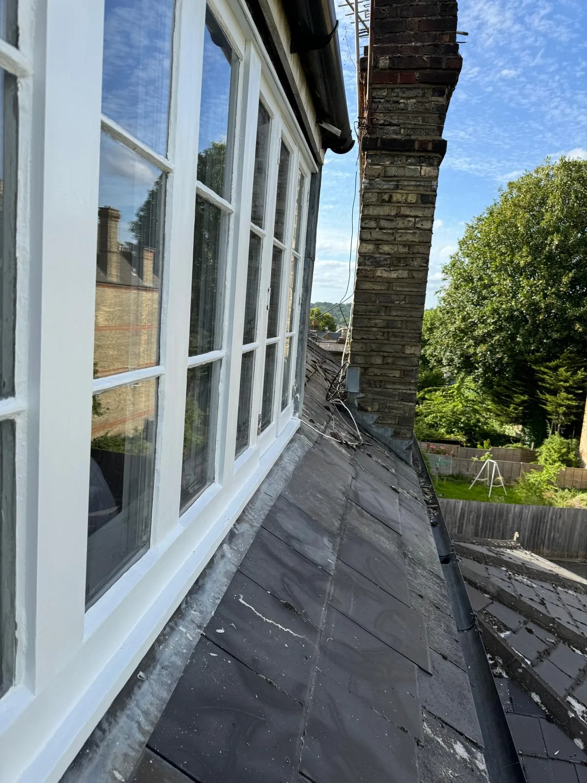 Restored white sash bay window with fresh gloss overlooking a London slate roof