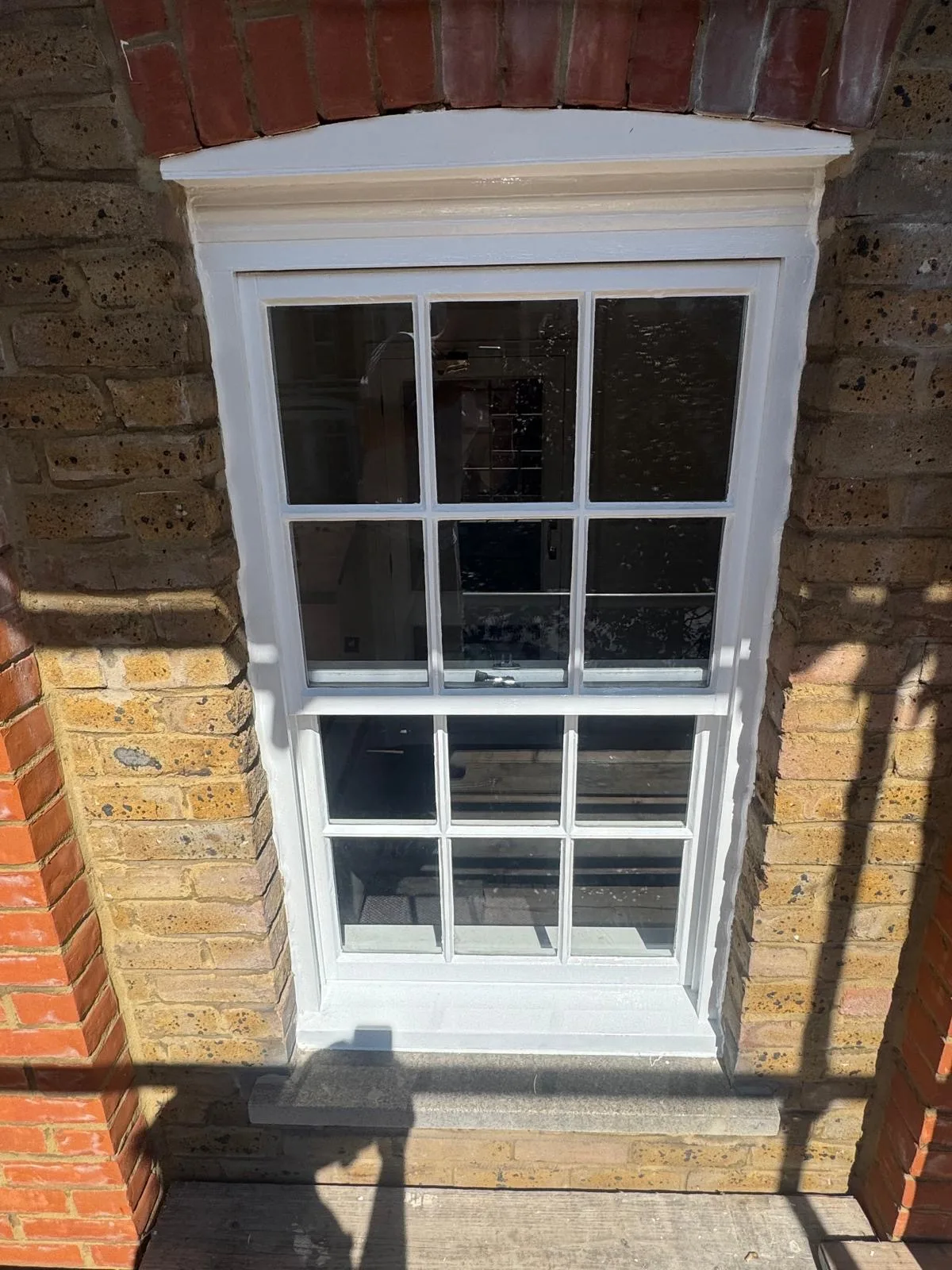 Repainted white sash window with brass hardware on a stock brick façade