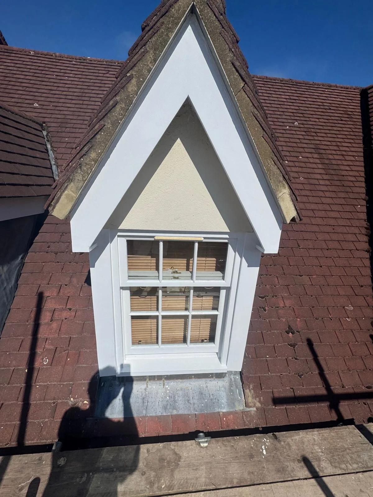 Freshly repainted gabled dormer sash window with crisp white trim on a tiled roof