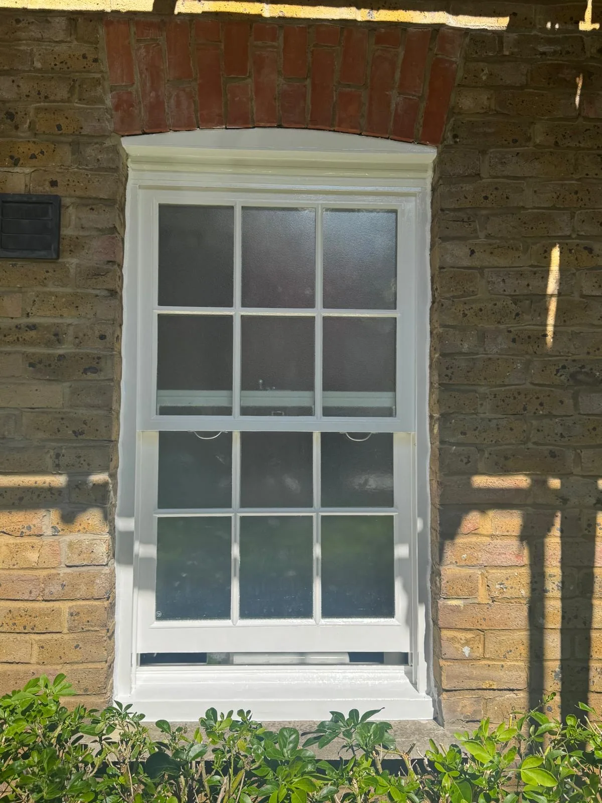 Restored sash window with obscured glass and red brick arch on a London façade