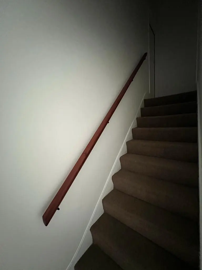 Stripped mahogany handrail on a repainted staircase wall